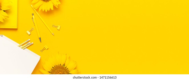 Top view flat lay of workspace desk styled design with sunflowers, white paper bag, pencils, pen, paper clips on bright yellow background. Autumn or summer Concept. Sunflower natural background. 