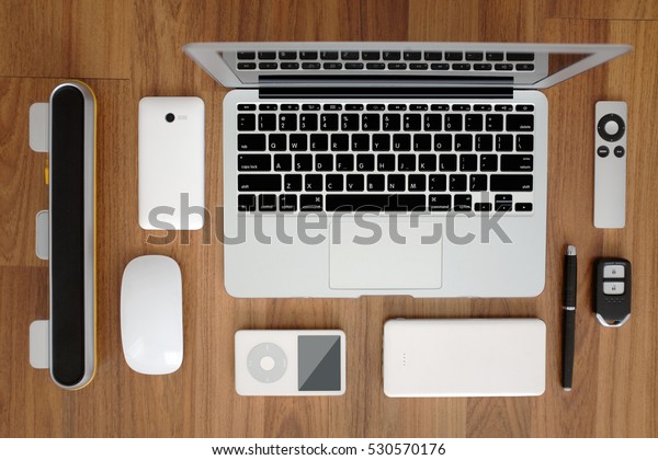 Top view\
flat layout of laptop computer with smartphone, remote, mouse,\
speaker, portable music player, battery pack, remote car key and a\
pen. Laptop with English keyboard. On wood\
top.