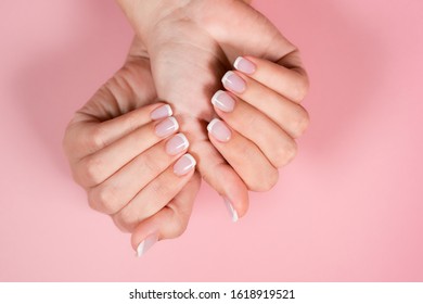 Top View Flatlay Closeup Photography Of Two Female Hands With Beautiful Classic French Pink And White Manicure. Fingers Isolated On Pastel Pink Background. Horizontal Color Image.