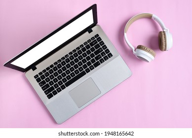 Top View Flatlay of modern wireless headphone and minimalist laptop with white screen on pink color workspace