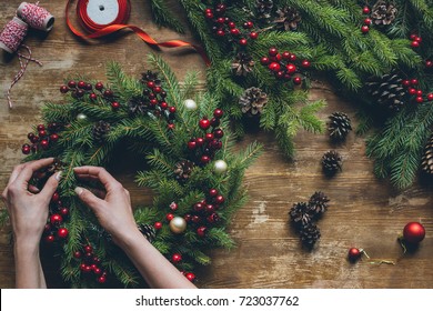 top view of florist hands making Christmas wreath on wooden tabletop