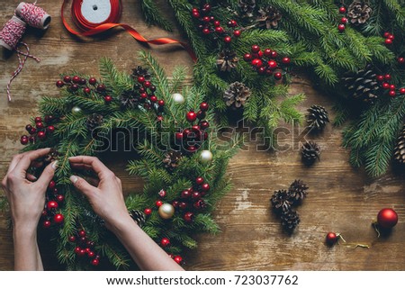 top view of florist hands making Christmas wreath on wooden tabletop