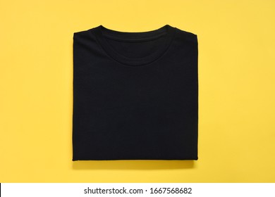top view of folded black color t-shirt on yellow background, copy space, flat lay