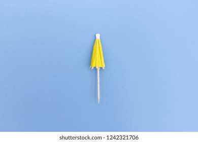 Top View Of Folded Cocktail Umbrella In Yellow Color On Blue Background