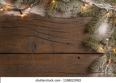 Top view of a frame made of snowy pine branches and Christmas lights placed on wooden table - Powered by Shutterstock