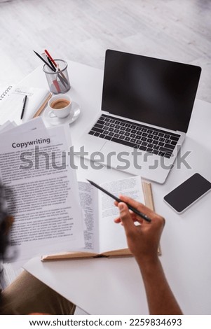 Top view of freelancer holding pencil and papers with copywriting lettering while working at home
