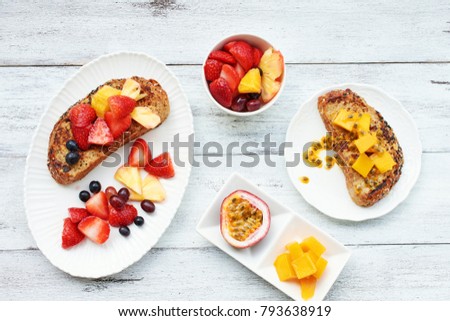 Top view of french toasts with strawberry, passion fruit, mango, grape and pineapple on white table. Healthy breakfast.