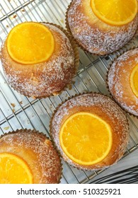 Top view of fresh bread rolls with a topping of sliced orange on a rack.