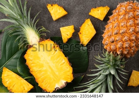 Top view of fresh cut pineapple with tropical leaves on dark gray table background.