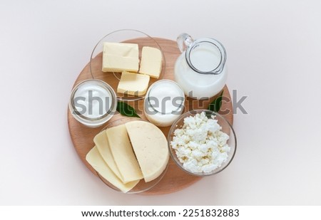 Top view of fresh dairy products: milk in a jug, cottage cheese, yogurt, sour cream and butter on a wooden round podium on a light background. Organic farm natural healthy food. Flat lay, close-up