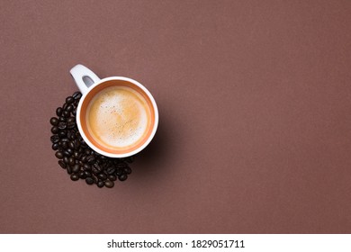 A top view of a fresh espresso cup surrounded by coffee beans on brown background