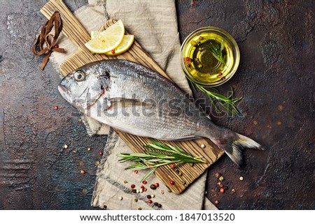 Top view of fresh fish dorado or gilt-head bream with lemon, olive oil and spices as pepper, rosemary on wooden cutting board and brown concrete background
