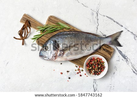 Top view of fresh fish dorado or gilt-head bream with spices as pepper, rosemary on wooden cutting board and white marble background