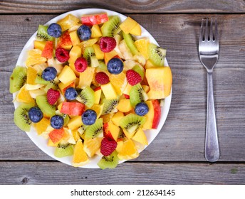 Top View Of A Fresh Fruit Salad With Bananas Kiwi Orange Blueberries And Peach On Plate With Fork On Wooden Table