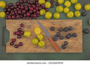 top view of fresh fruits such as red cherriesgreen cherry plumsdark purple sloes on a wooden kitchen board with knife with red cherries isolated on a green background - Powered by Shutterstock