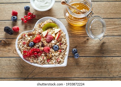 Top view of fresh honey and yogurt placed on wooden table near heart shaped bowl of muesli with pieces of fruits and berries in morning - Powered by Shutterstock