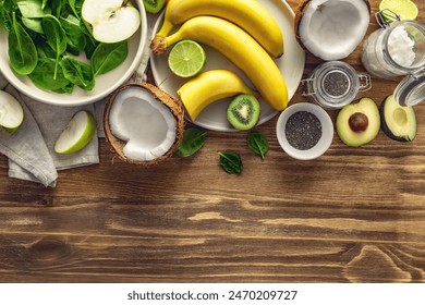 Top view of fresh ingredients for cooking a green smoothie bowl of bananas, avocado, spinach, apple, kiwi, lime, coconut and chia seeds on a wooden background with copy space - Powered by Shutterstock