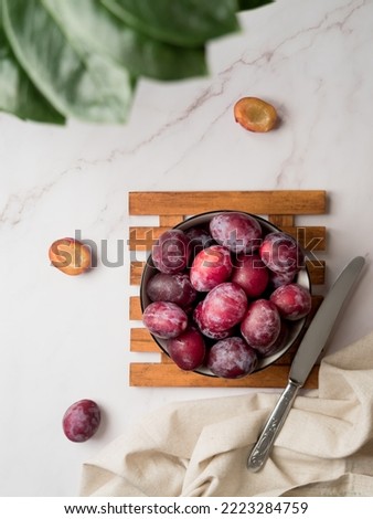 Top view of fresh plum fruits in a deep plate on a white marble kitchen table. Flat lay. Place for text