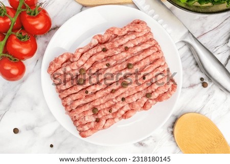 Top view of fresh raw minced meat with peppercorns on plate. Ingredients for cooking meal, tomatoes, broccoli, garlic on marble table. Uncooked gound pork, beef.