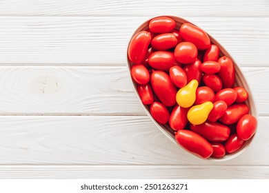 Top view of fresh red grape tomatoes with a single yellow tomato in a bowl on a white wooden background. - Powered by Shutterstock