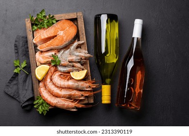 A top view of fresh seafood such as shrimp, langoustines, and trout steaks, accompanied by white and rose wine