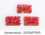 Top view of fresh strawberries packed in clear plastic containers arranged on a white background. The vibrant red strawberries with green leaves create a visually appealing display of fresh produce.