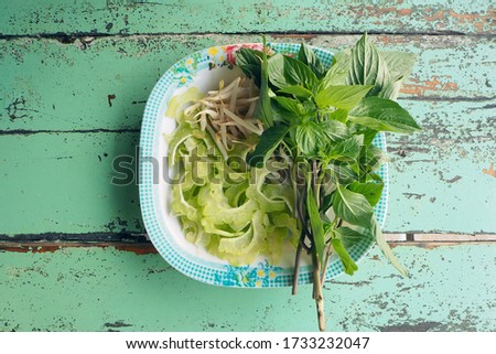 top view of fresh vegetable set; sweet basil, bitter melon and bean sprout side dish on old wooden green table in Thai noodle resturant.