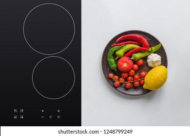 Top View Of Fresh Vegetables On Plate And Electric Stove