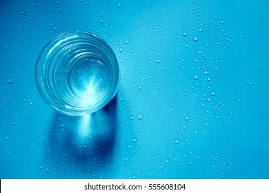 Top View Of Fresh Water In A Glass With Water Drops On Blue Background.