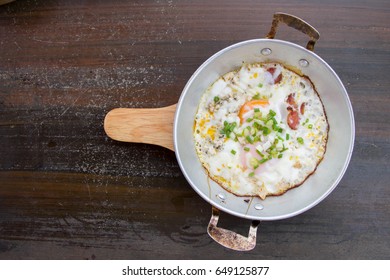 top view of fried eggs in pan with sausage and spring onions for breakfast on dark table