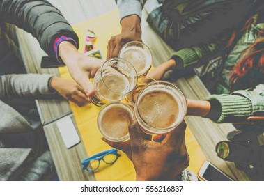 Top view of friends cheering with home brew in pub bar restaurant - Young people hands toasting and beers half pint - Friendship and party concept - Warm matte filter - Focus on bottom hand
