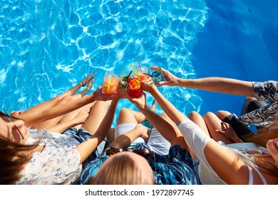 Top view of of friends clinking glasses with fresh colorful cocktails sitting by swimming pool on sunny summer day. People toast drinking beverages at luxury villa poolside party on tropical vacation. - Powered by Shutterstock