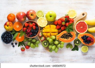 Top view of fruits, strawberries, blueberries, mango, orange, grapefruit, banana, apple, grapes, kiwis on the white background, copy space for text, selective focus