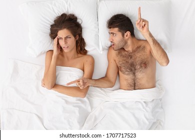 Top View Of Frustrated Wife Has Headache Because Of Husbands Yelling, Angry Annoyed Man Points Above And Sideways, Tries To Persuade Woman, Demands To Follow His Rules, Pose In Comfortable Bed