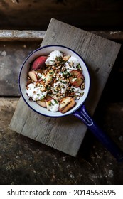 A Top View Of A Frying Pan With Grilled Red Potatoes, Greens, Nuts, And Sour Cream