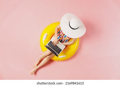 Top view full body young woman in striped swimsuit lies on inflatable rubber ring pool hold use work on laptop pc computer isolated on plain pink background. Summer vacation sea rest sun tan concept - Powered by Shutterstock