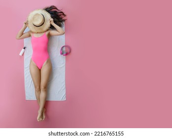 Top view full body young woman wearing pink swimsuit cover face with hat lies on white towel in pool isolated on plain pastel pink background. Summer vacation sea rest sun tan concept.