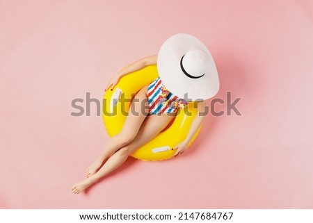 Top view full body young woman wearing striped swimsuit cover face with hat lies on inflatable rubber ring in pool isolated on plain pastel pink background. Summer vacation sea rest sun tan concept