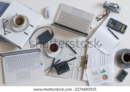 Top view of a full business desk with laptops, accounting papers, calculator, coffee and other office supplies, success work or stress concept, high angle shot from above, selected focus