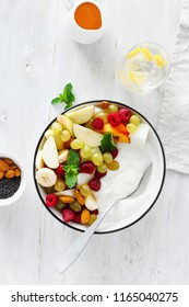 Top view full fruit breakfast and natural yoghurt bowl. Grapes, peach, apple, melon, raspberry, almond, honey and greek yogurt. Healthy food concept on white background, flat lay