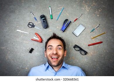 Top View Funny Photo Of Businessman With Beard Wearing Shirt. Businessman Cheerfully Smiling And Lying On Floor Full Of Office Supplies