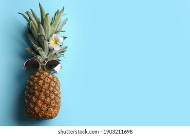 Top view of funny pineapple with sunglasses and plumeria flower on light blue background, space for text. Creative concept