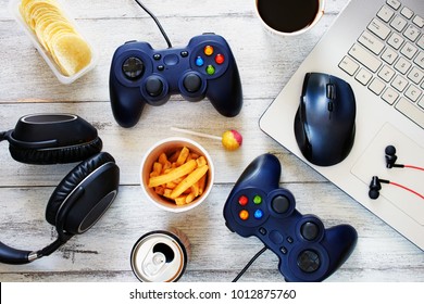 Top View Of Gamer Background. Gamepads, Headphone, Laptop With Mouse Pad And Snacks Over White Table.