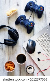 Top View Of Gamer Background. Gamepads, Headphone, Laptop With Mouse Pad And Snacks Over White Table.