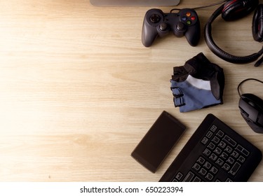 Top View Gaming Gear, Mouse , Keyboard, Headset, Gaming Gloves, Gamepad, Smartphone On Wooden Desk Table.