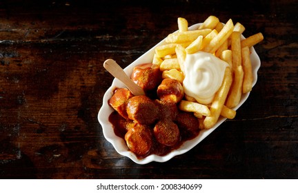 Top view of German curried sausage chunks with appetizing deep fried potato sticks and mayo in bowl on brown background - Powered by Shutterstock