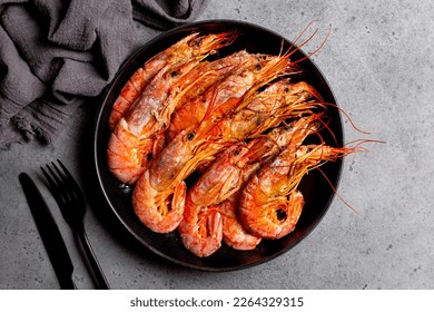 Top view of giant argentinian red prawns, grilled. Black plate. Dark grey background.