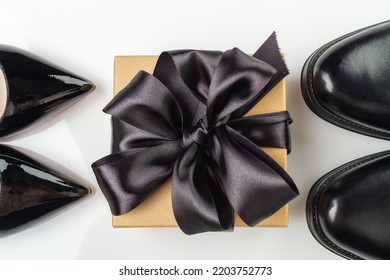 Top View Of Gift Box With Black Ribbon And Shoes. Classic Mens And Womens Footwear Isolated On White.