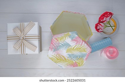 top view of gift boxes and red color roses with rolls of adhesive tape and pink ribbon on white wooden background - Powered by Shutterstock