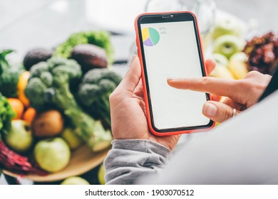 Top View Of Girl Holding Smartphone With Calorie Counting App On Kitchen Table Near Fresh Vegetables. 